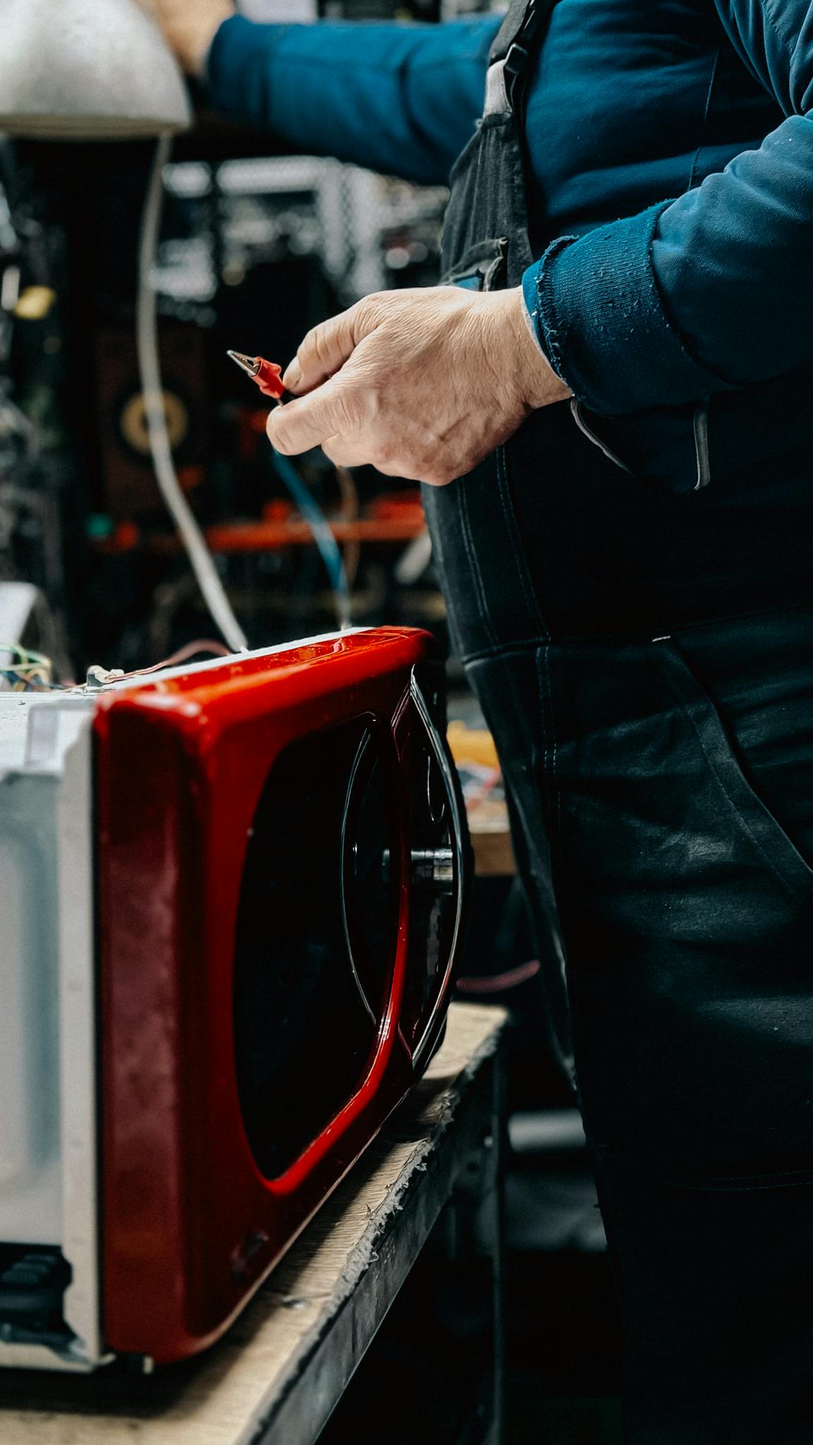 Servicio de mantenimiento y repación en toda España - Reparaciones de electrodomésticos Electrician working on red microwave repair in a workshop setting, tools in hand.