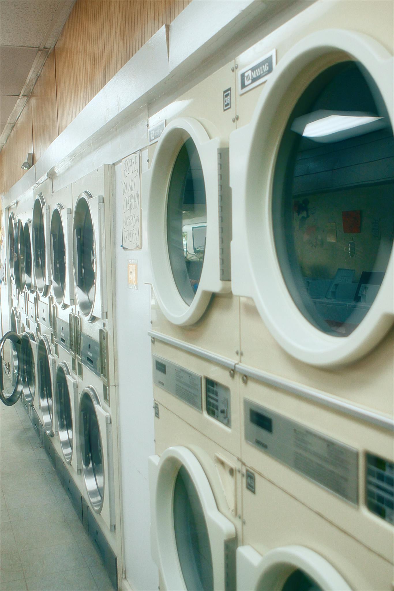 Servicio de mantenimiento y repación en toda España - Reparaciones de electrodomésticos Interior view of a clean and organized laundromat with multiple washing machines lined up.